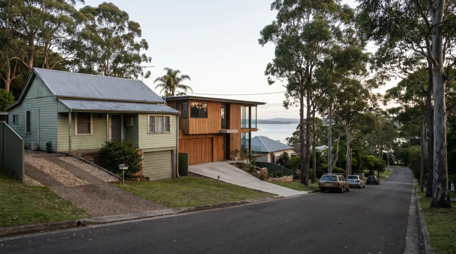 A steep Coal Point street with driveways dropping to under-house garages and a glimpse of Lake Macquarie between houses