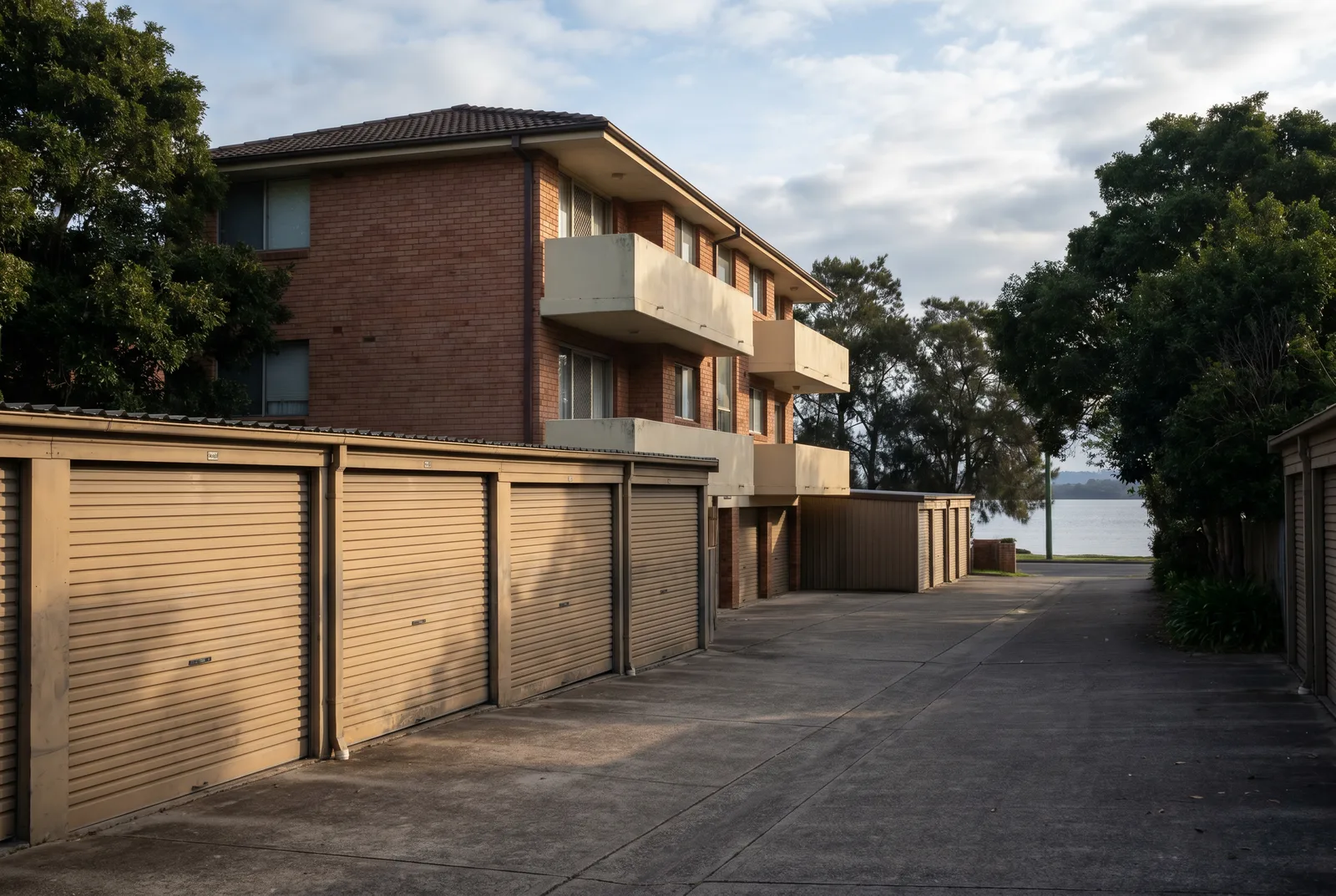 A row of roller doors on single garages behind a small older walk-up unit block, morning light across the corrugated curtains