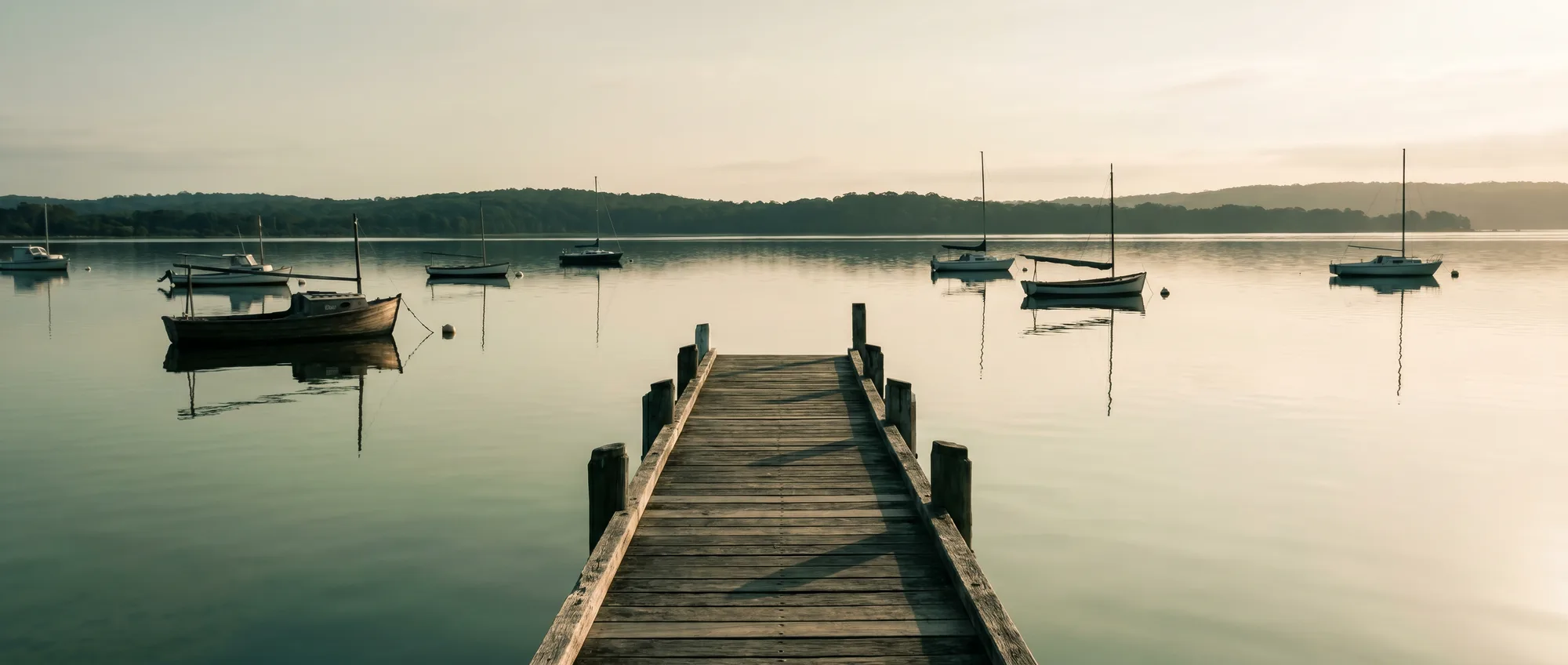 The still surface of Lake Macquarie at dawn from the Toronto foreshore, a timber jetty reaching into pale green-grey water